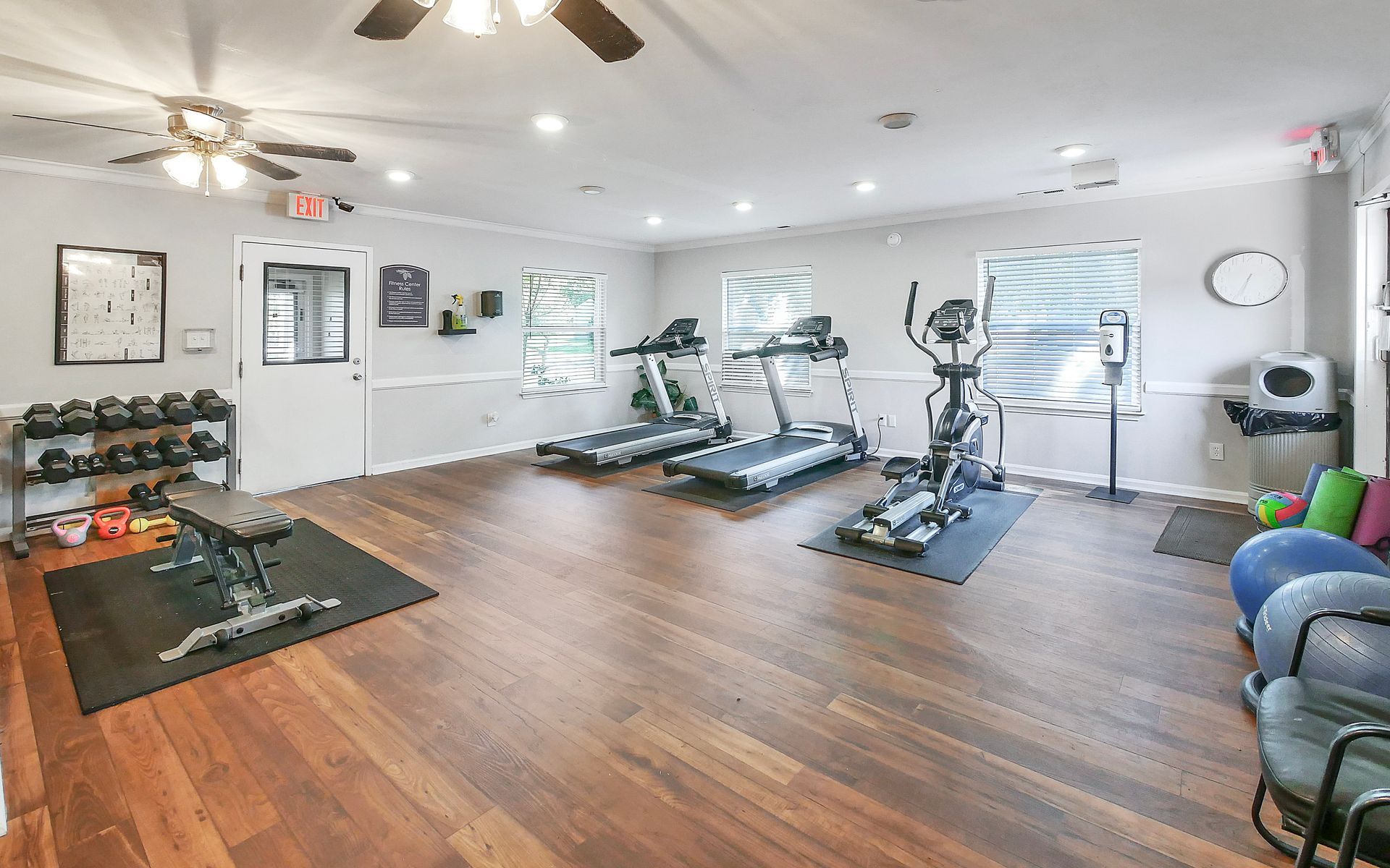 A gym featuring two treadmills, an elliptical machine, a rack of dumbbells, a weight bench, and exercise balls.