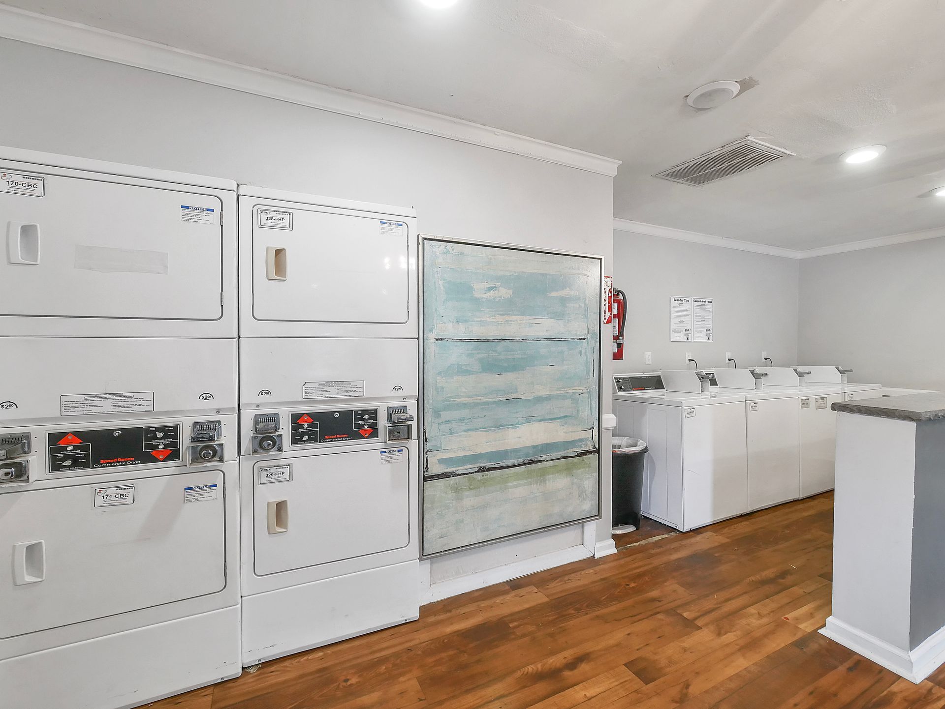 A clean laundry room featuring white stacked washers and dryers along one wall and a row of washers against the back.