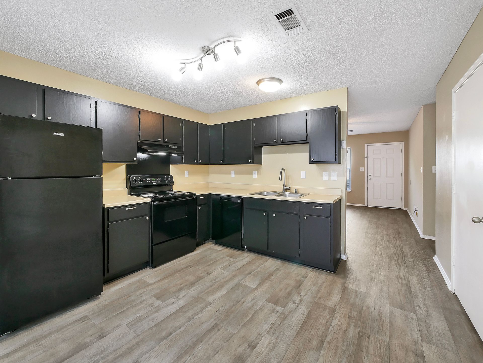 A kitchen with black cabinetry, a matching black refrigerator and stove, light-colored countertops, and wood-look floors.