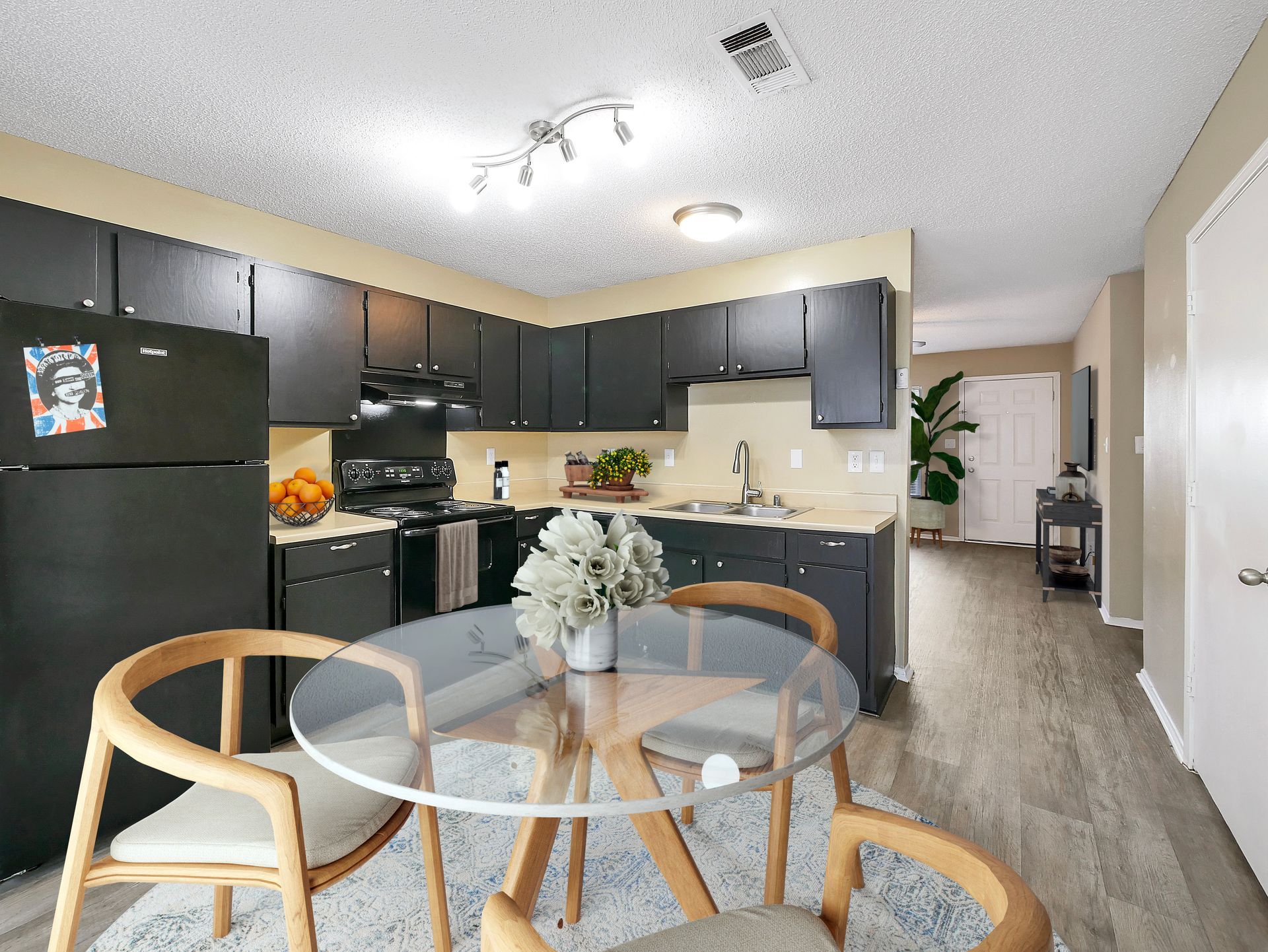 Kitchen with black cabinets and appliances, a glass-topped dining table with chairs, and light wood flooring.