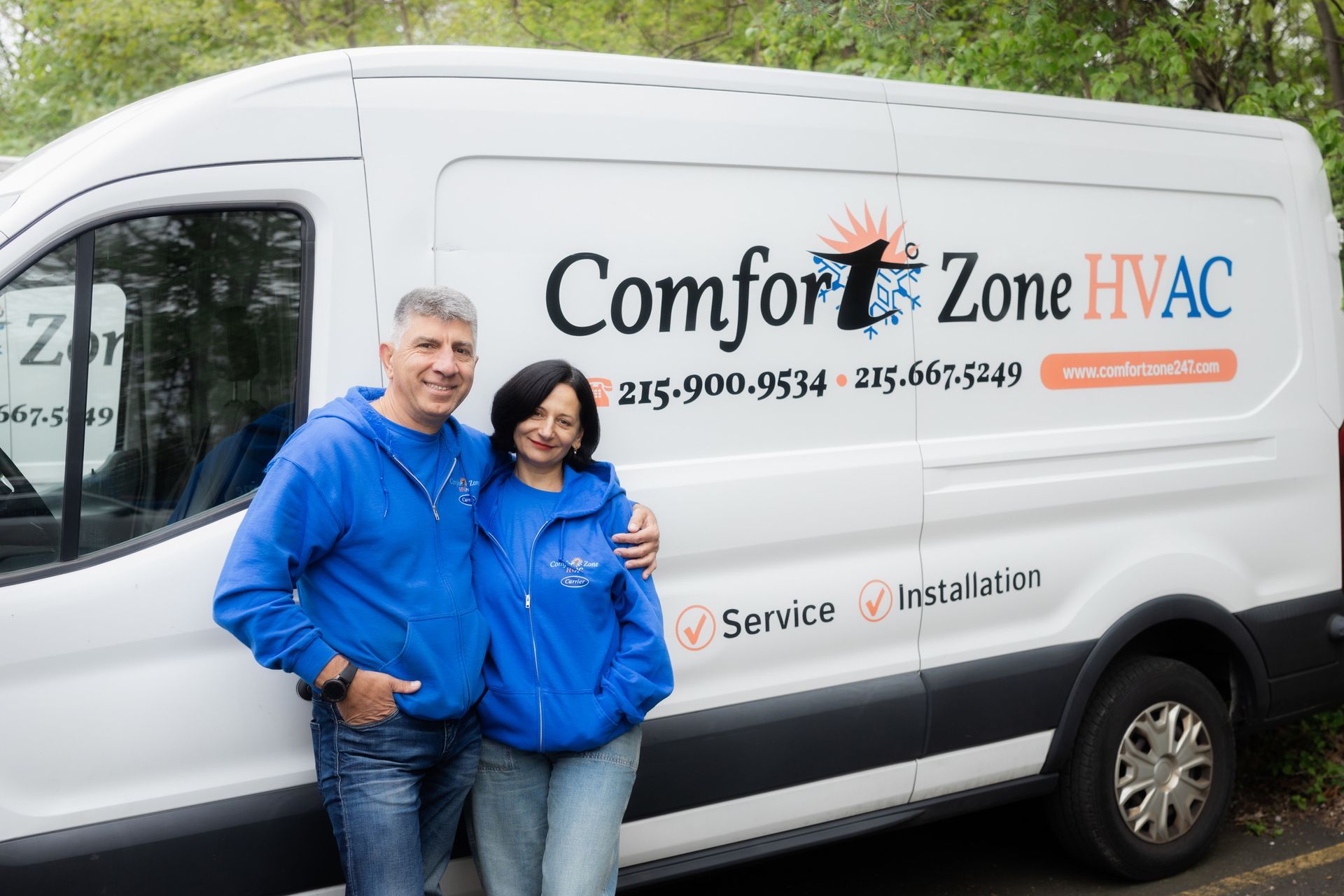 A man and woman are standing in front of a comfort zone hvac van.