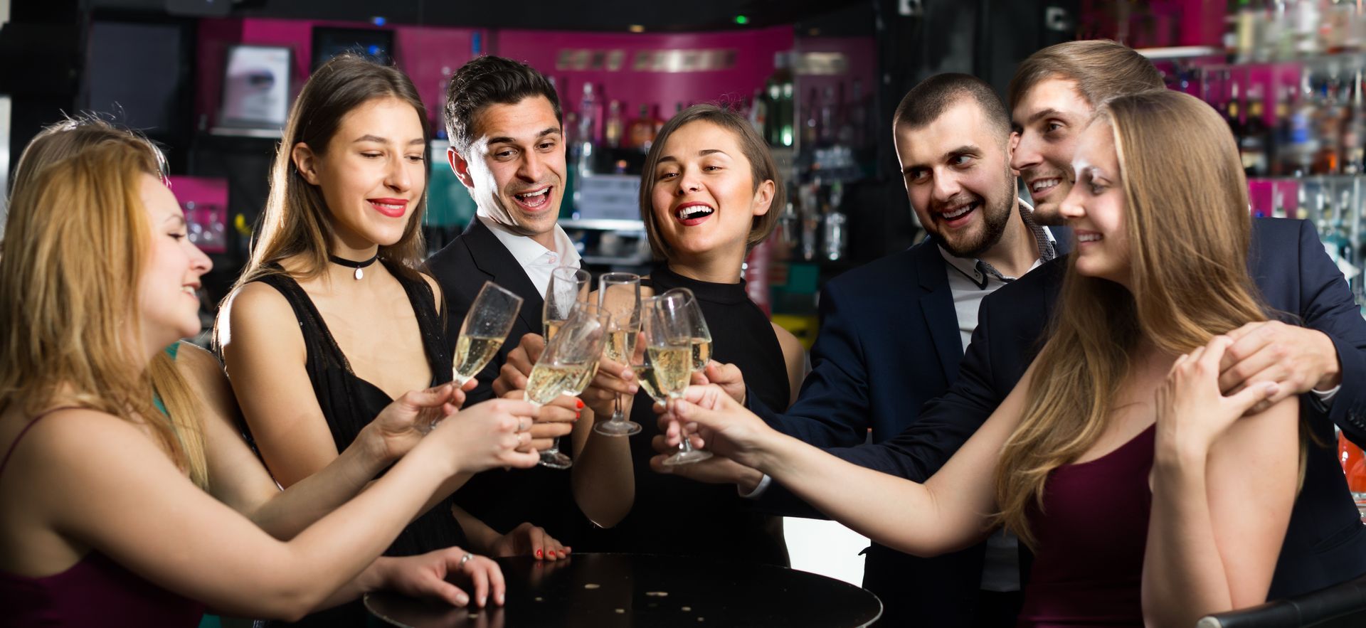 Group of friends toasting drinks at a lively bar, smiling and chatting under colorful lights