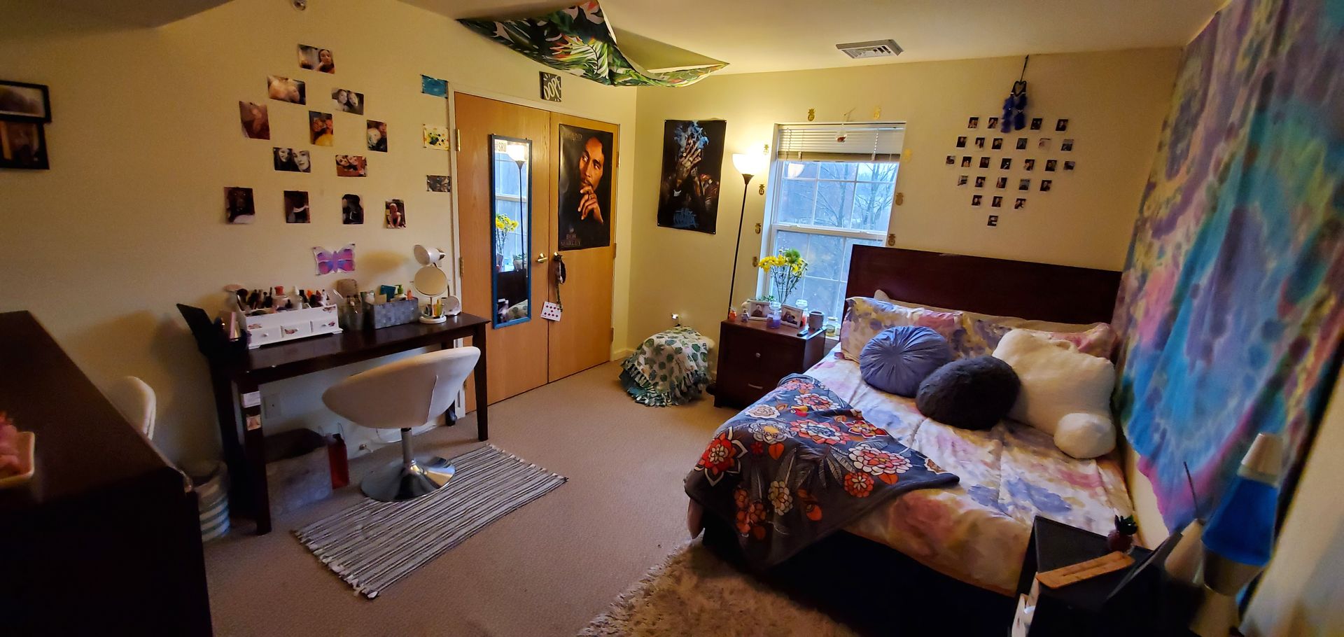A bedroom with a bed , desk , chair and paintings on the wall.