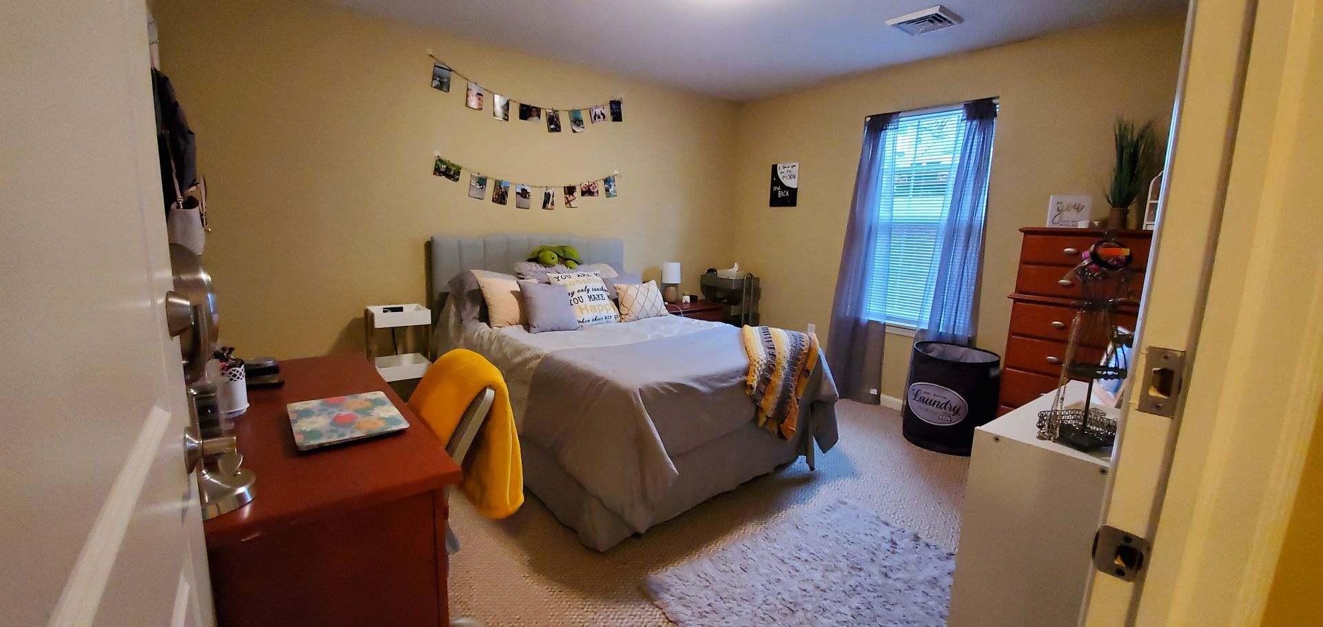 A bedroom with a bed , desk , dresser and window.