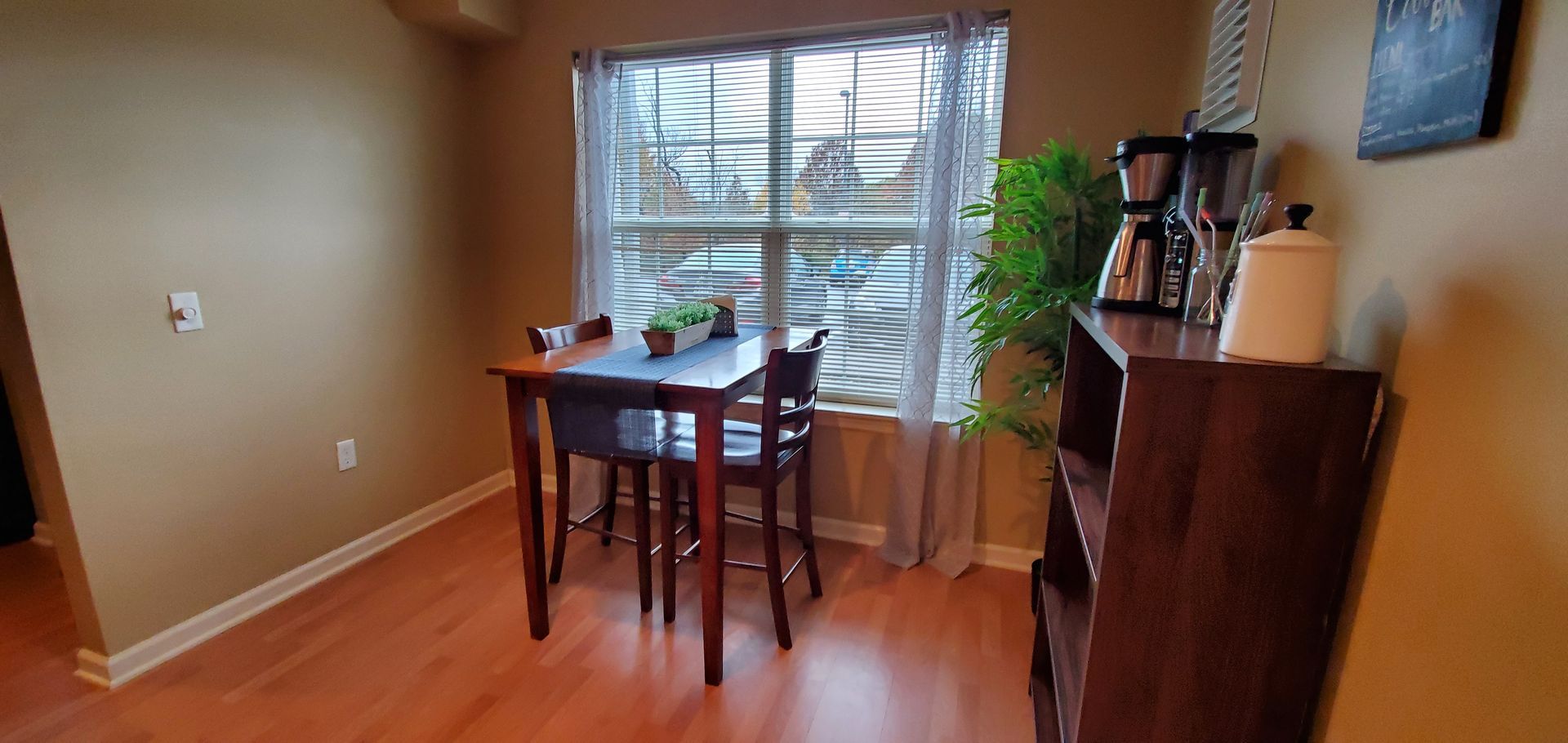 A dining room with a table and chairs in front of a window.