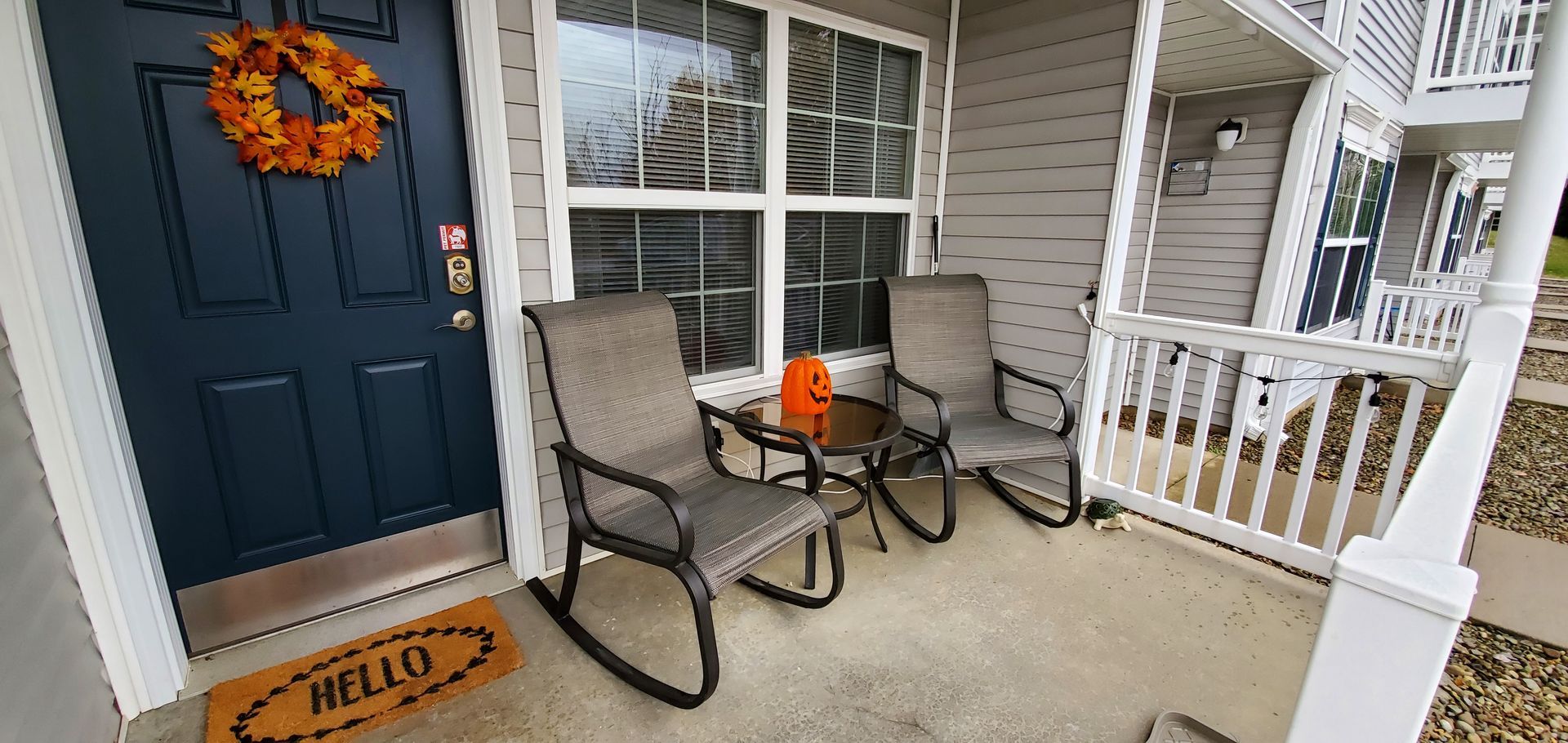 A porch with rocking chairs , a table , and a hello doormat.