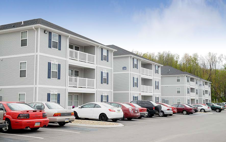A row of cars are parked in front of a large apartment building.