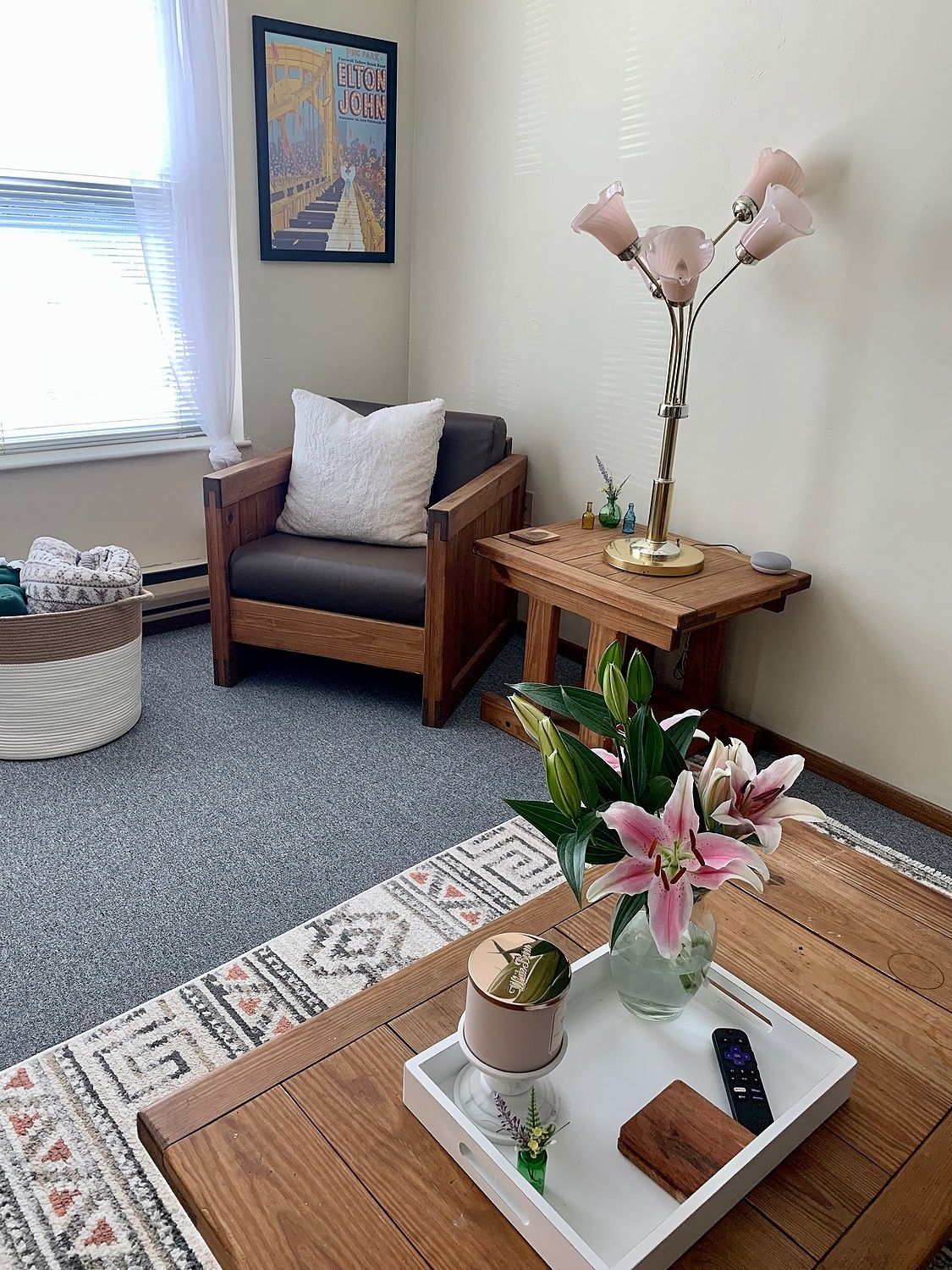 A living room with a coffee table , chair , lamp and flowers on it.