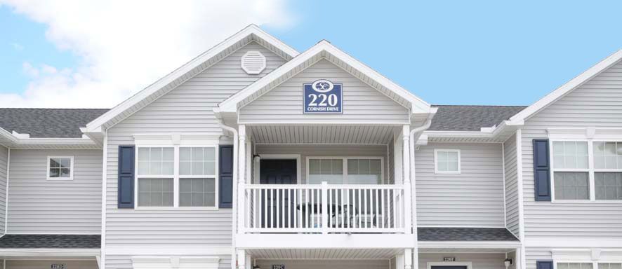 A white apartment building with a balcony and a blue sign that says 220.