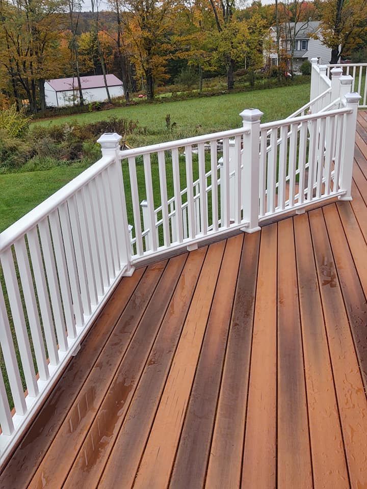 White railed deck overlooking a green yard with a small white shed in the distance, autumnal trees.