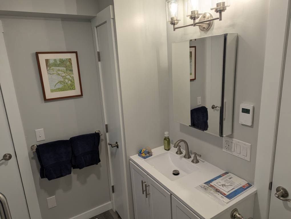 Small bathroom with sink, mirror, and two dark blue towels on a bar.