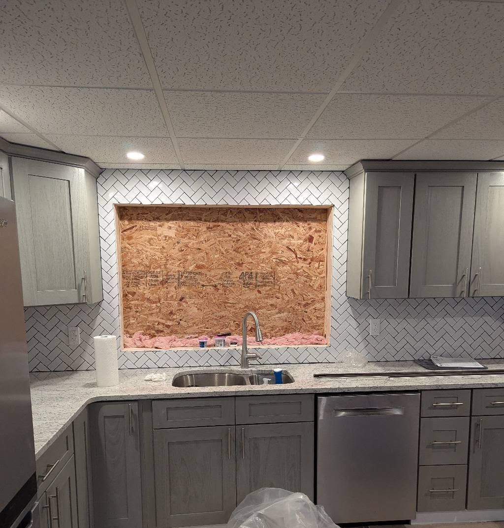 Kitchen under renovation with light gray cabinets, tile backsplash, and unfinished window.