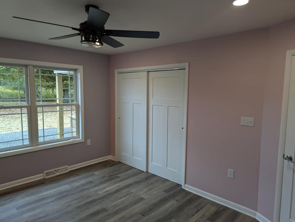 Bedroom with pink walls, white closet doors, gray flooring, and a ceiling fan.