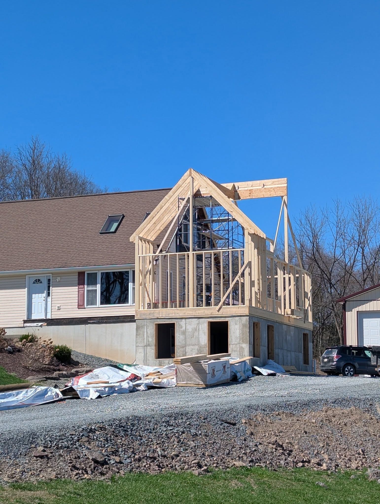 Construction site: wood frame addition to a house, against a clear blue sky.