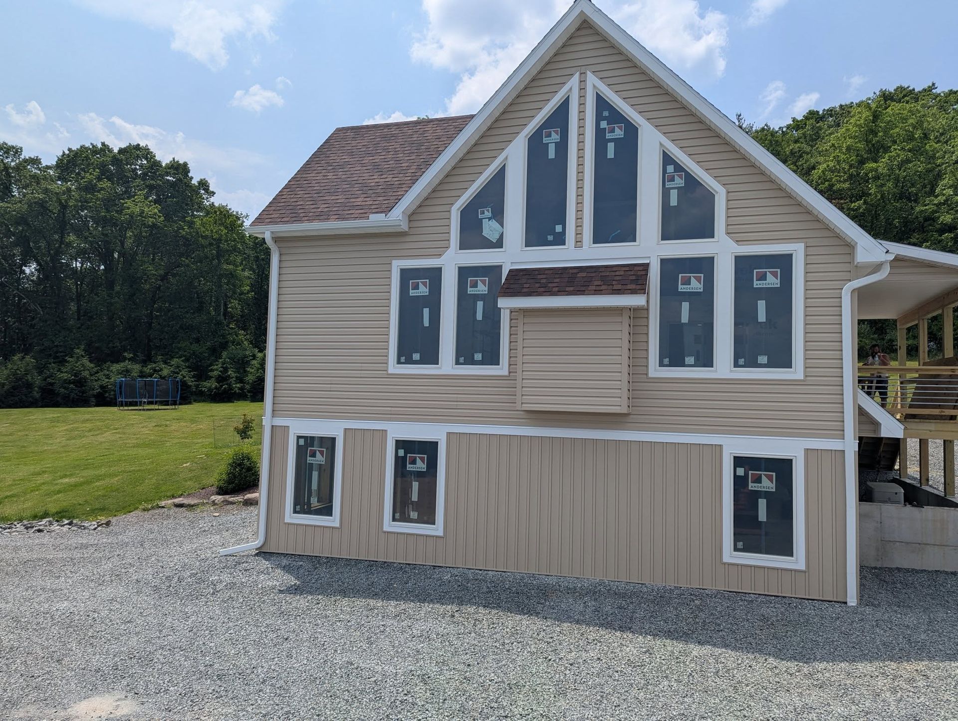 Beige house with many windows covered in protective film, gravel driveway, grassy lawn, blue sky.