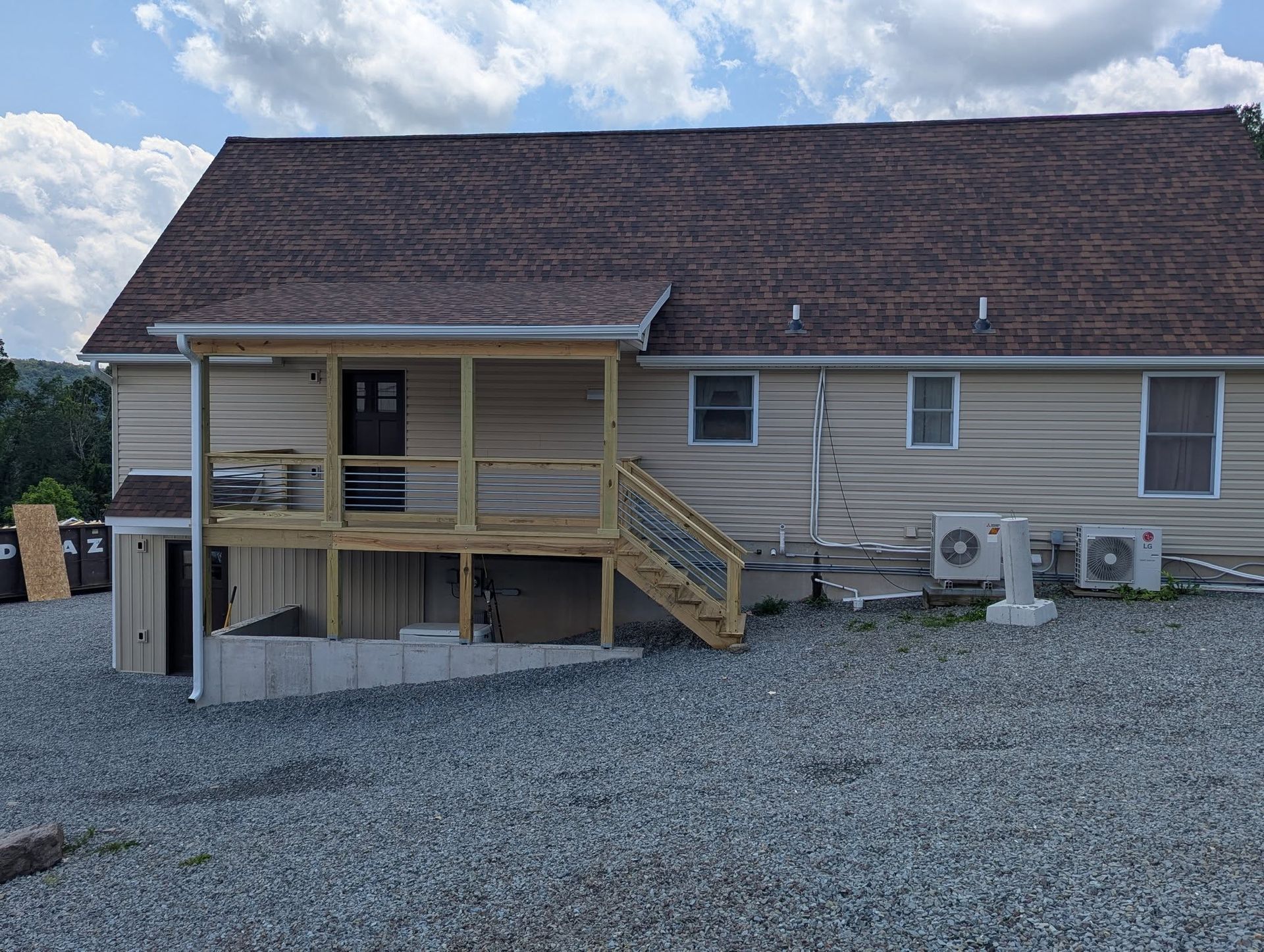 Tan building with porch and stairs, gravel ground, air conditioning units, and a cloudy sky.