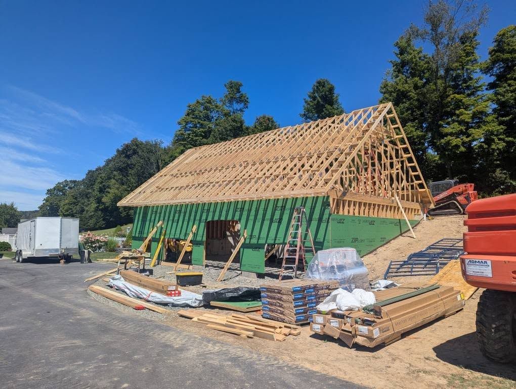 Construction of a wooden building with green siding and a partially built roof against a blue sky.