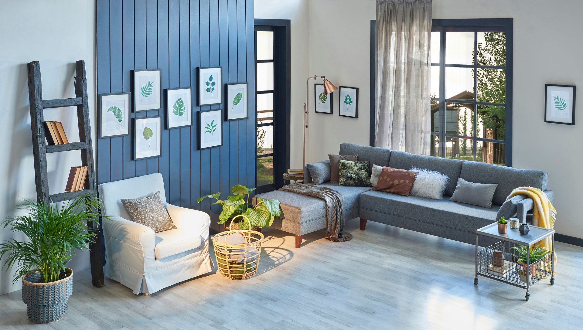 Living room with blue accent wall, gray sectional sofa, plants, framed art, and wooden ladder.