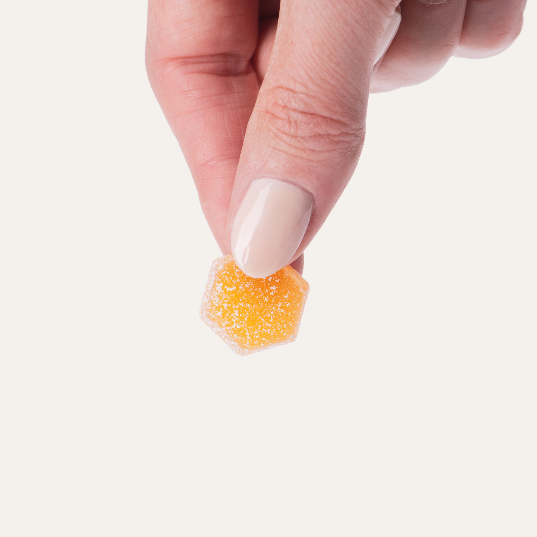 A person is holding a piece of orange candy in their hand.