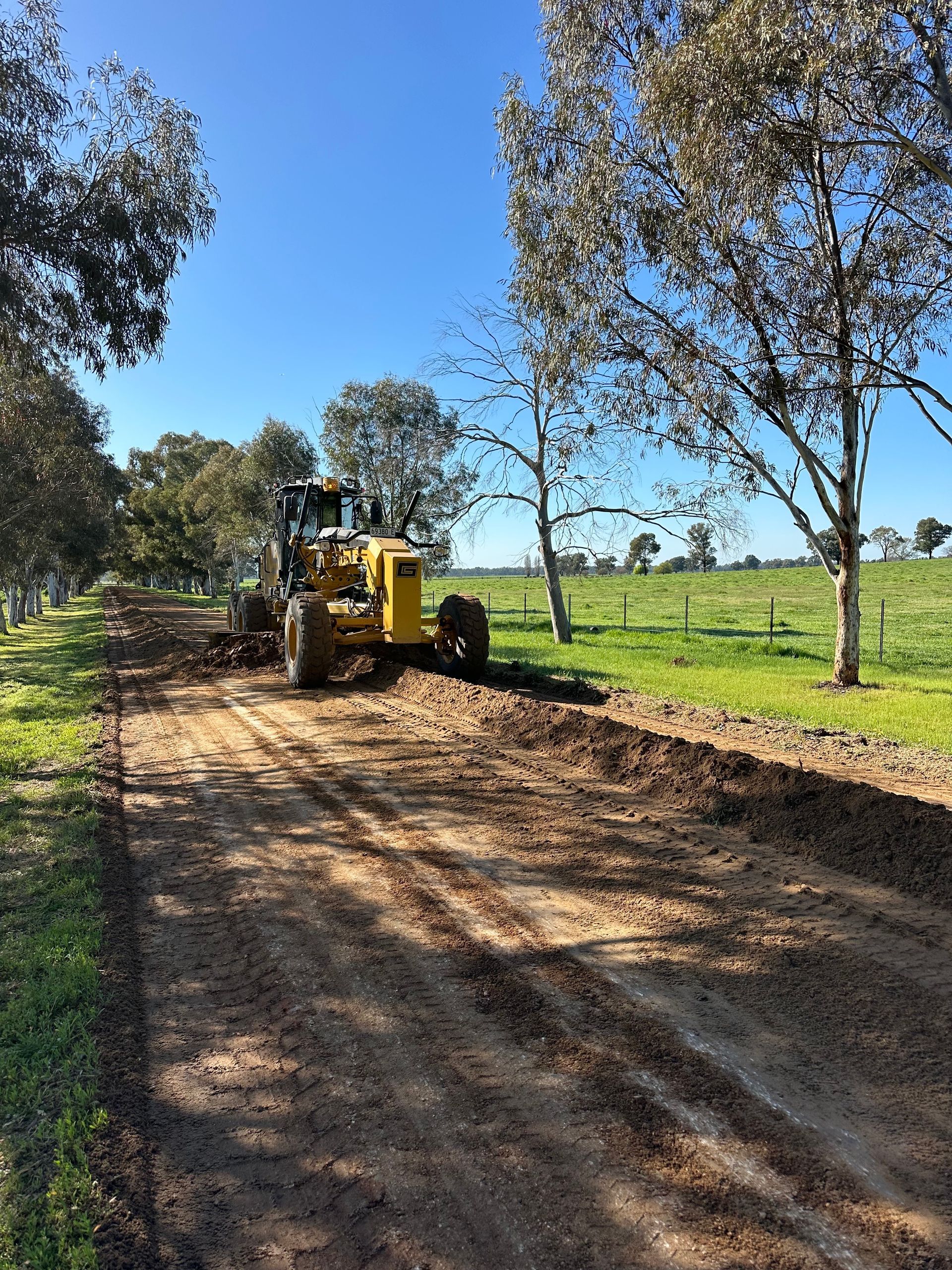 Grader performing maintenance on a rural farm road, ensuring smooth access with expert civil & agricultural earthworks.