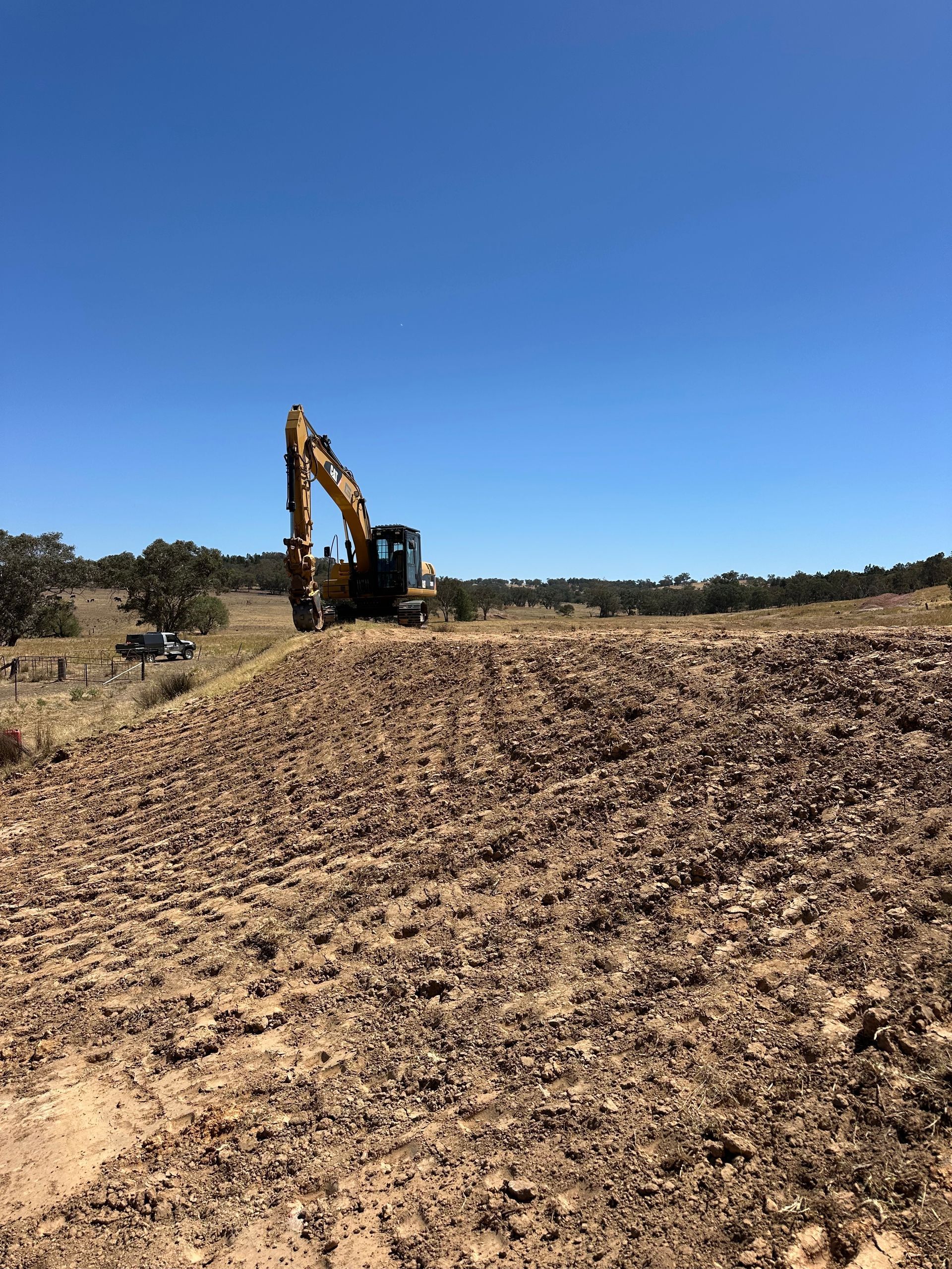 Excavator working on a recently cleaned and repaired dam bank, expert earthmoving for agricultural water management.