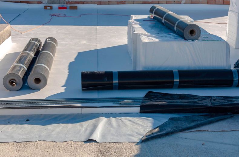Matériaux de toiture en rouleaux et outils étalés sur un toit plat sous un soleil éclatant
