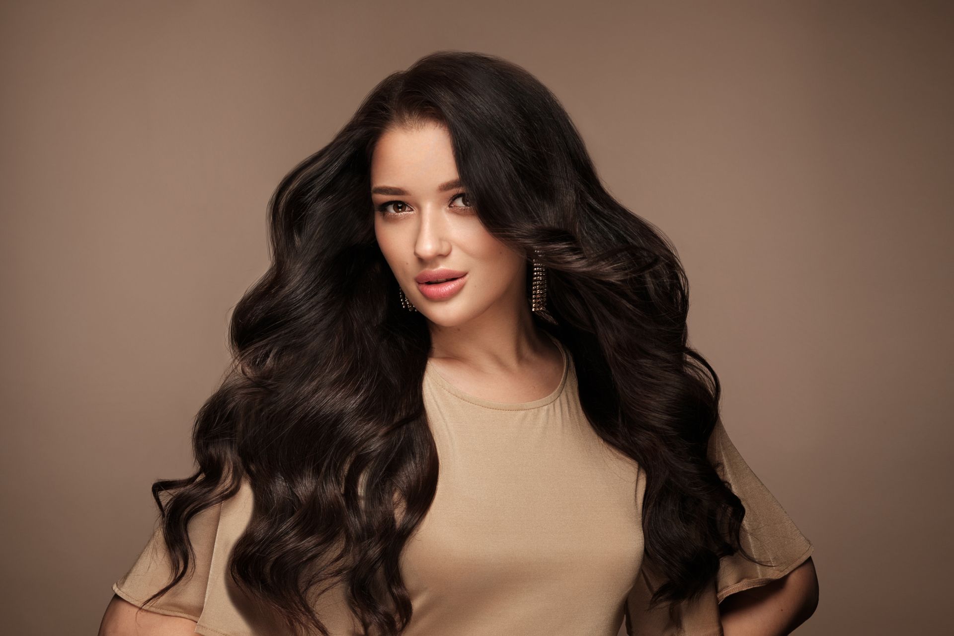 A woman with long dark hair is standing in front of a brown background.