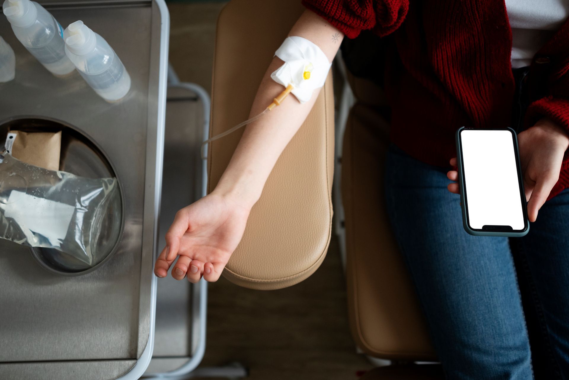 A woman is sitting in a hospital chair with an iv in her arm and holding a cell phone.