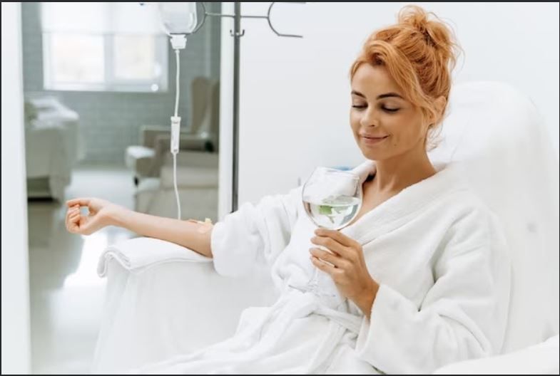 A woman is sitting in a hospital bed holding a glass of water.