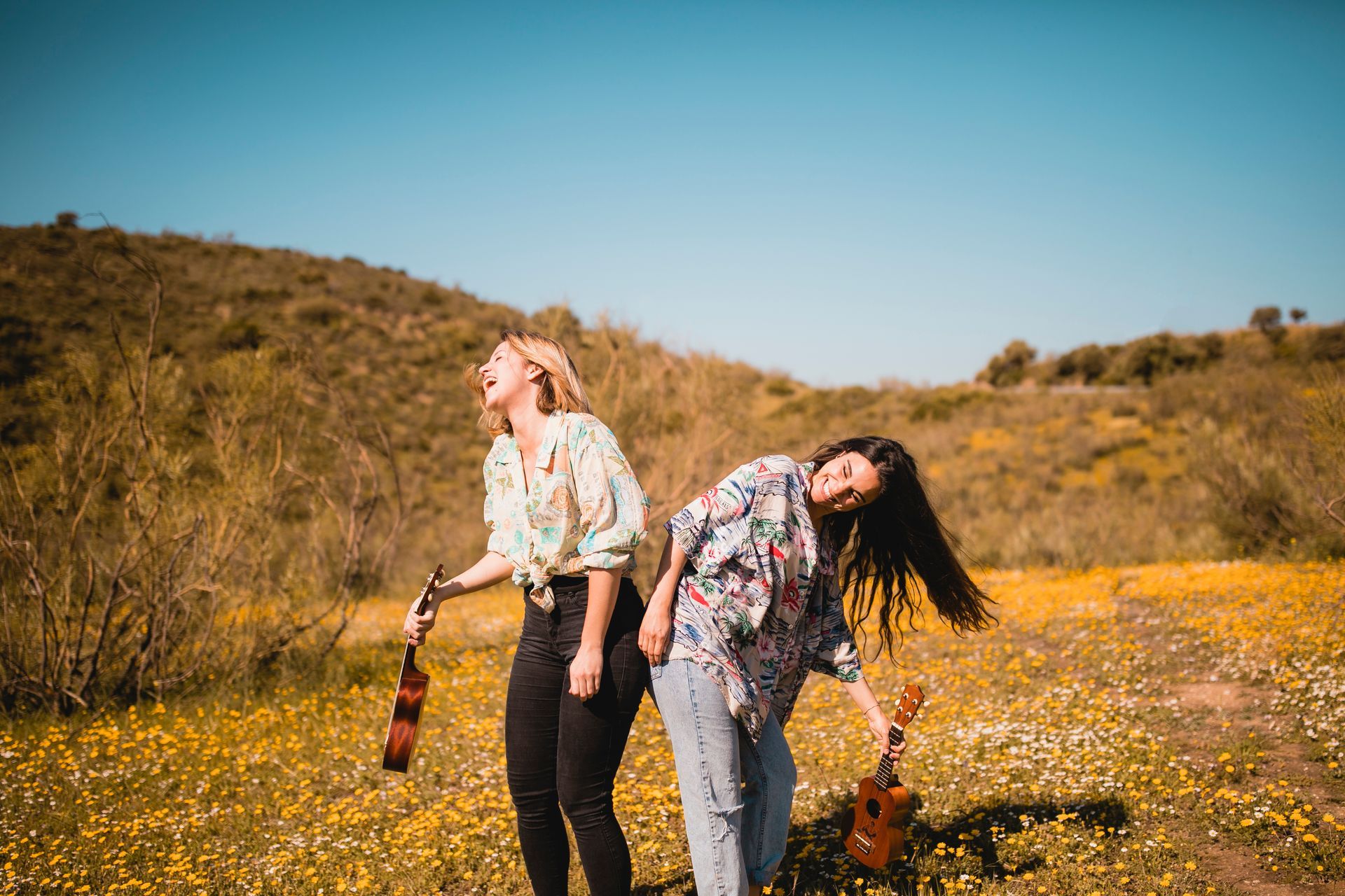 Two women are standing in a field of flowers holding ukuleles.