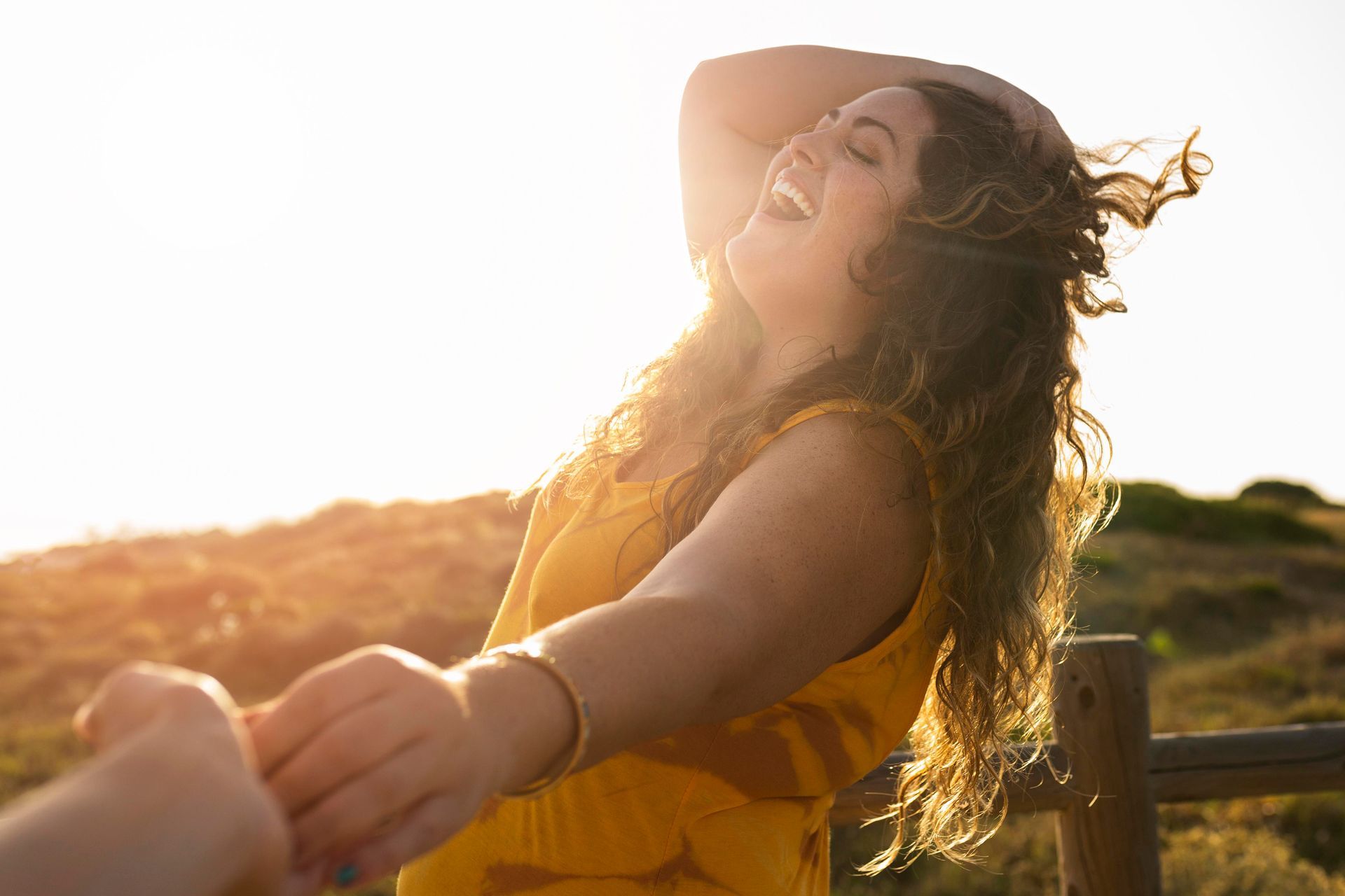 A woman in a yellow dress is holding a man 's hand and laughing.