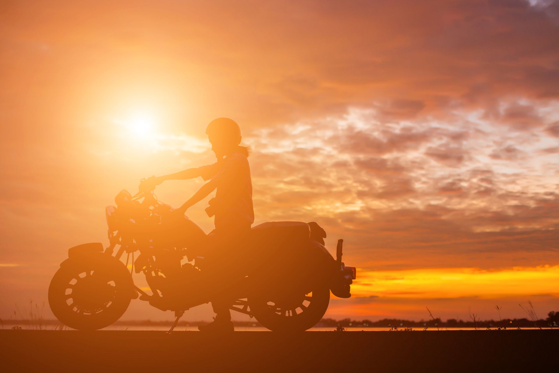 A man is riding a motorcycle on a road at sunset.