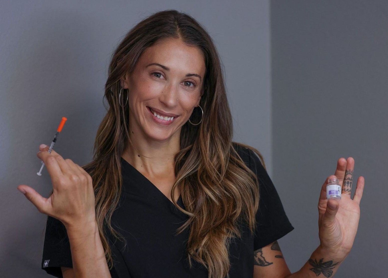 A woman is smiling while holding a syringe and a bottle.