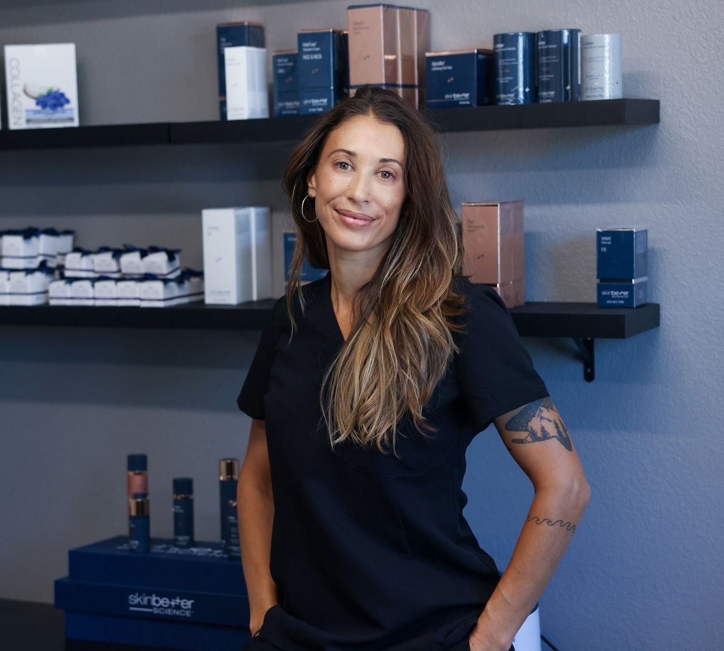 A woman in a black shirt is standing in front of a shelf with cosmetics on it.