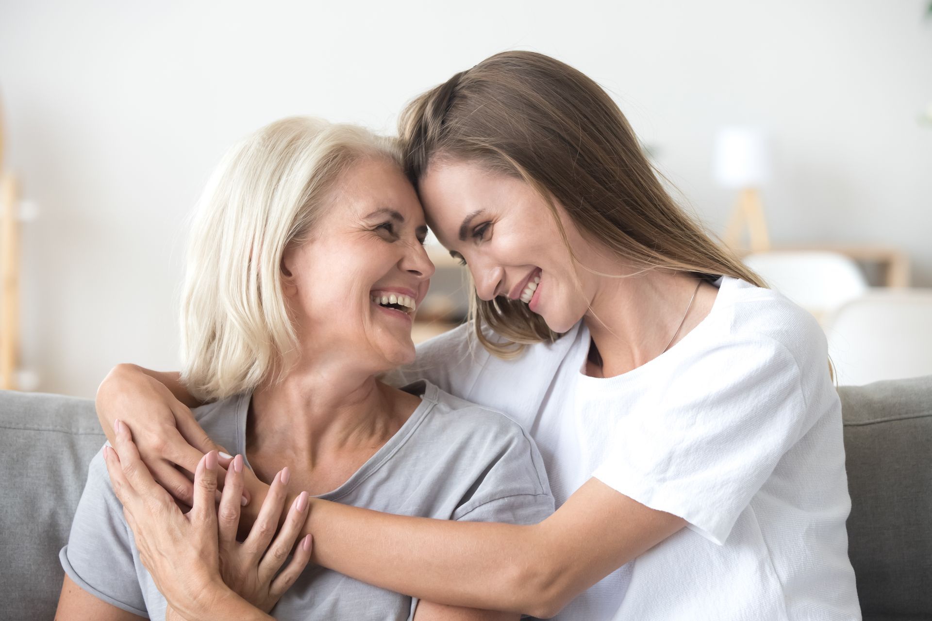 Two women smiling and hugging on a couch in a bright living room