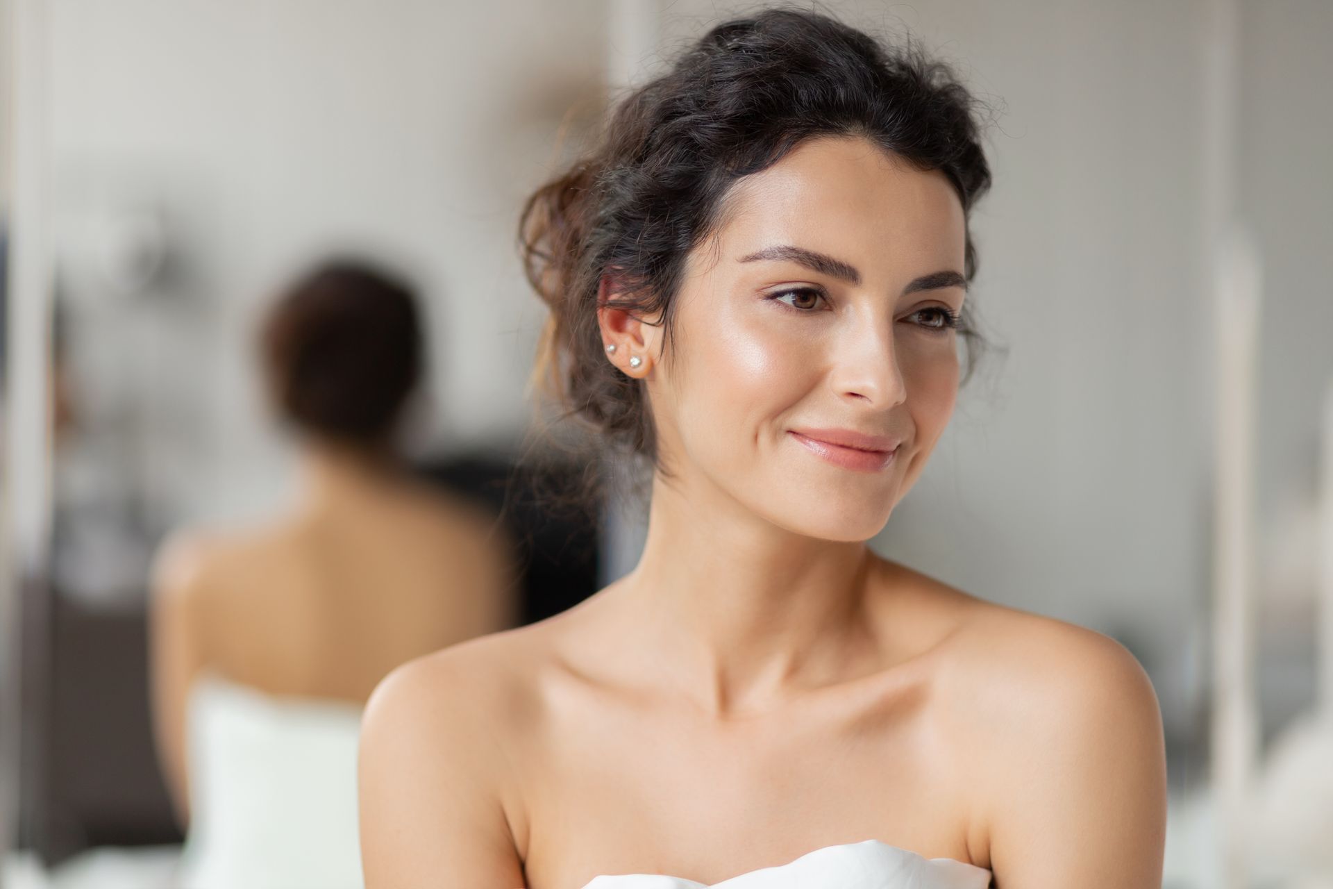 A woman in a white dress is smiling in front of a mirror.