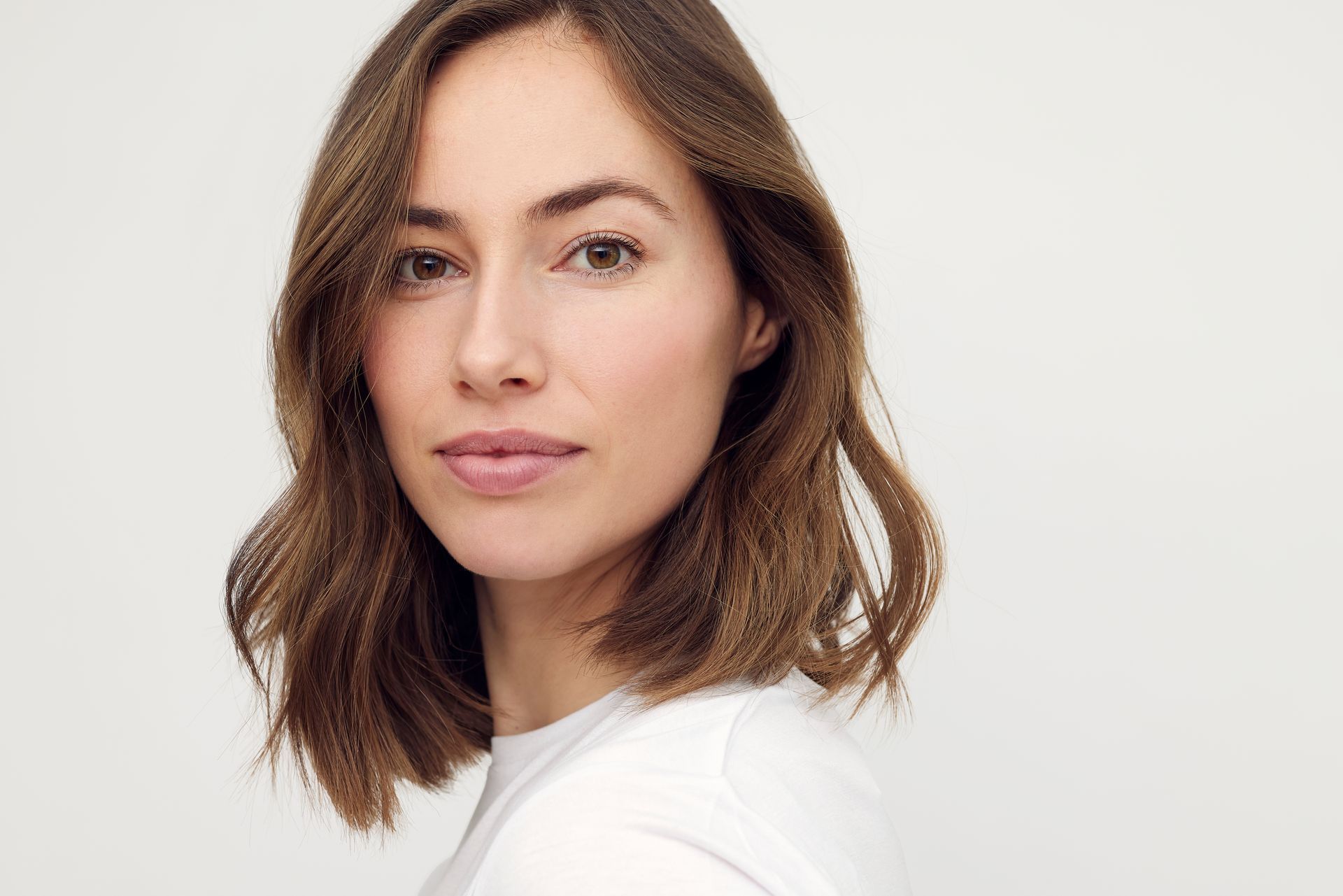 A woman with short brown hair is wearing a white shirt and looking at the camera.