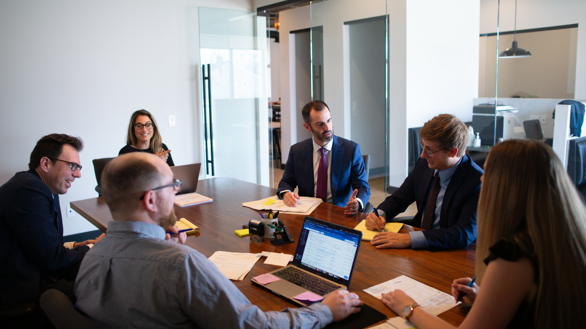 A group of people are sitting around a table with laptops.