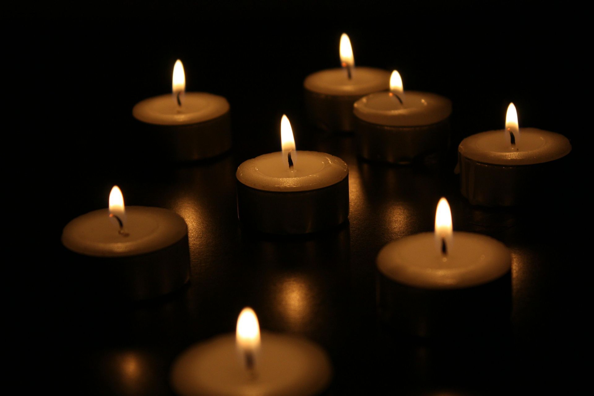 Lit tea light candles glow against a dark background, reflecting warm light.