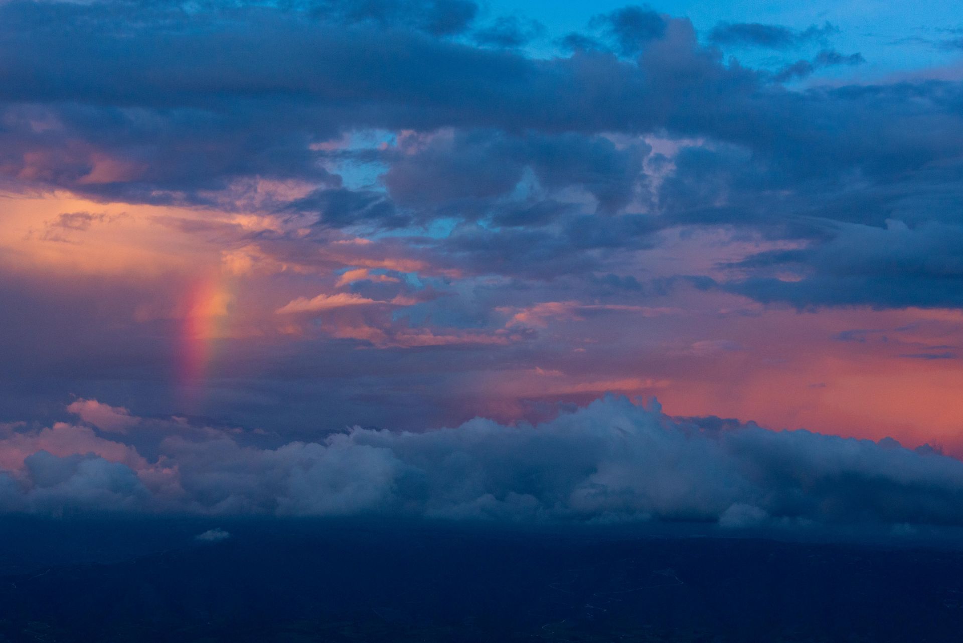 Rainbow arcs across a vibrant sunset sky, visible through dark blue and white clouds.