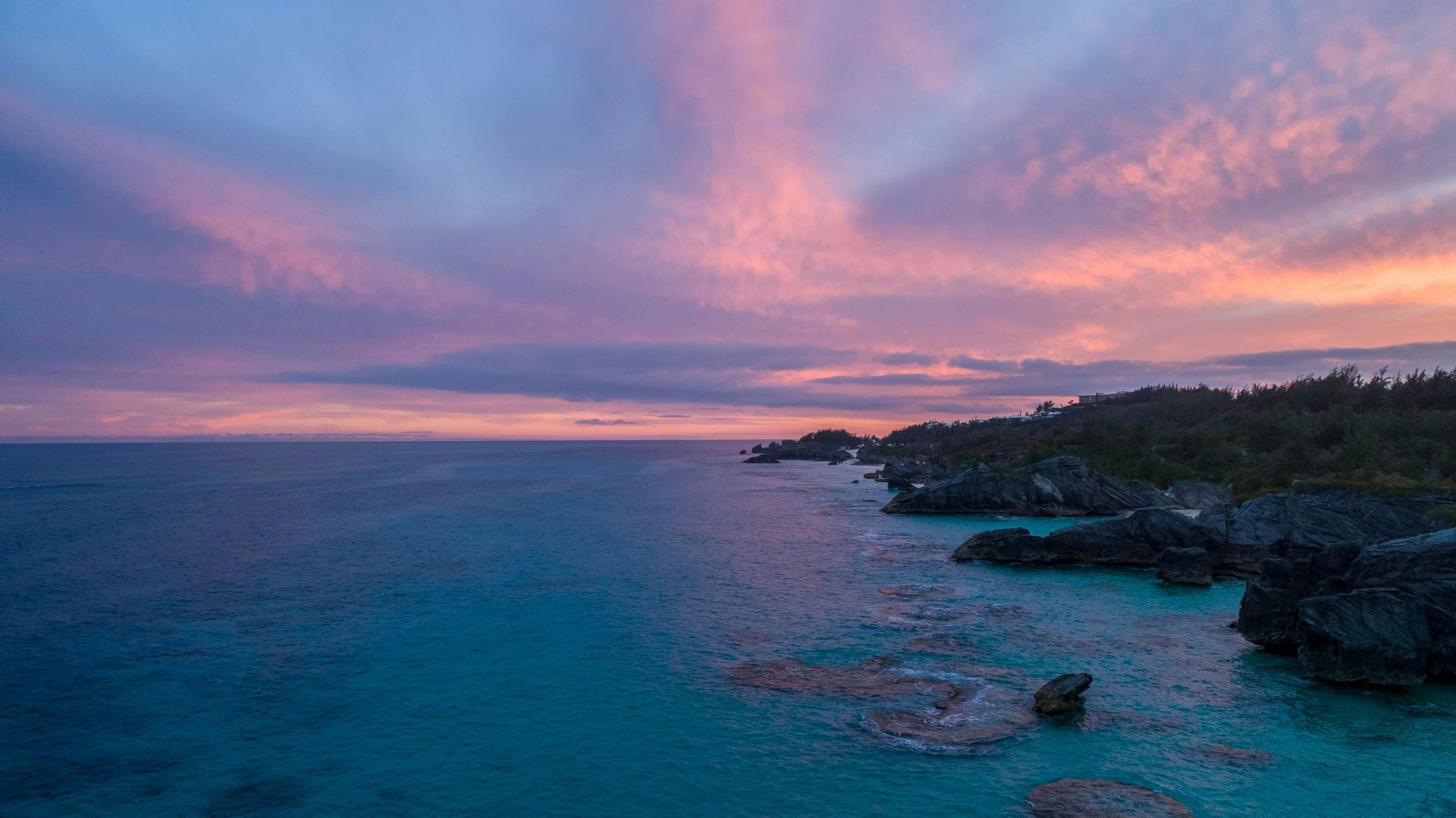 Ocean coastline at sunset with pink and purple clouds.