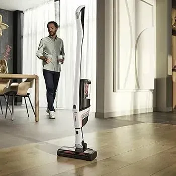 Slim white vacuum cleaner in a modern room, with a person walking in the background.