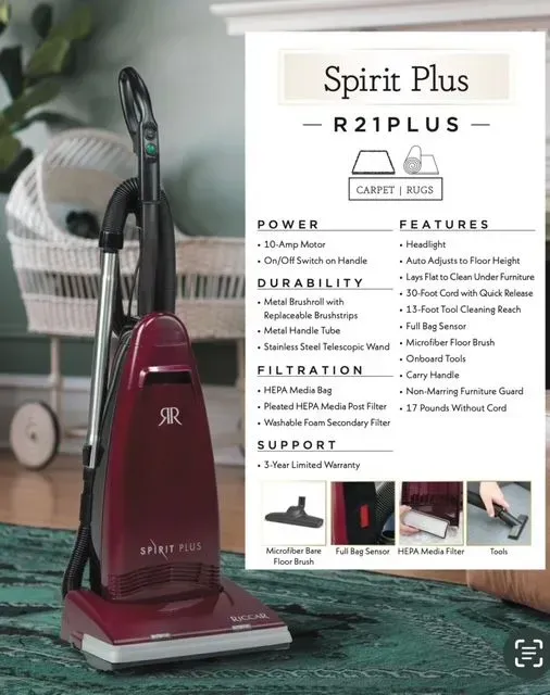 Maroon upright vacuum cleaner beside product box labeled Spirit Plus R21PLUS on a green rug.