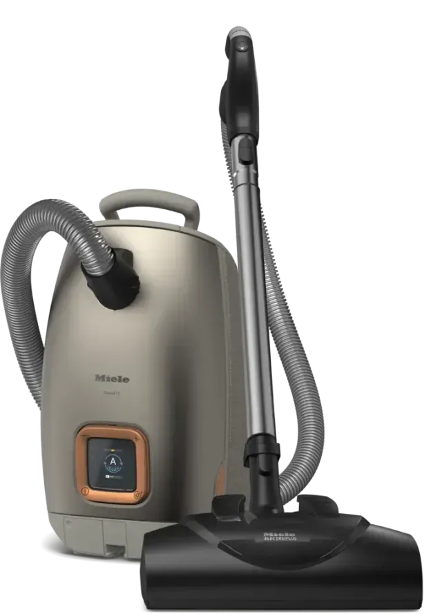 Beige canister vacuum cleaner with black hose and floor nozzle on white background
