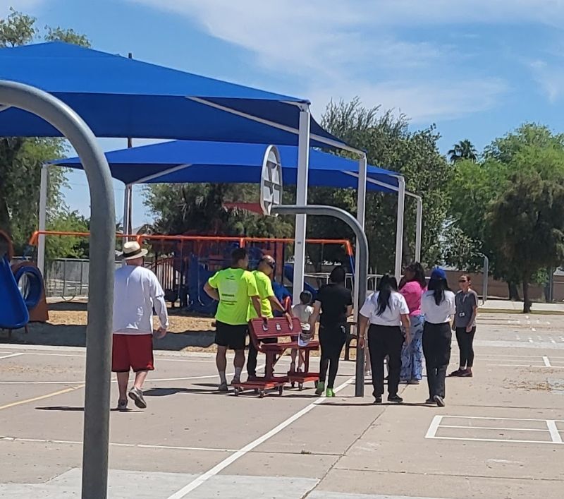 People gather on a basketball court under a blue shade structure.