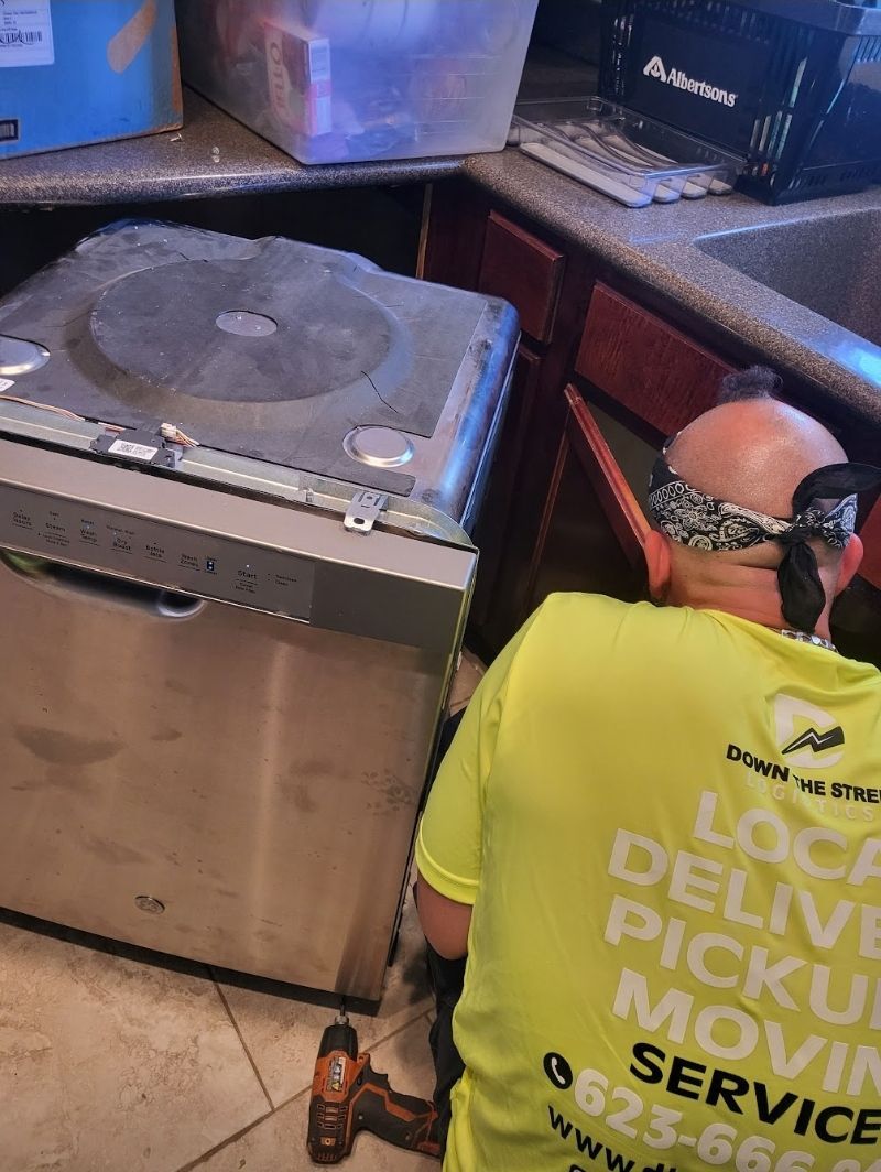 Man in yellow shirt, removing a dishwasher from a kitchen cabinet.