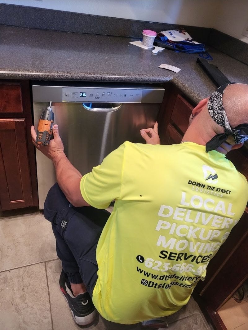 Person working on a dishwasher, wearing a blindfold. Kitchen setting.