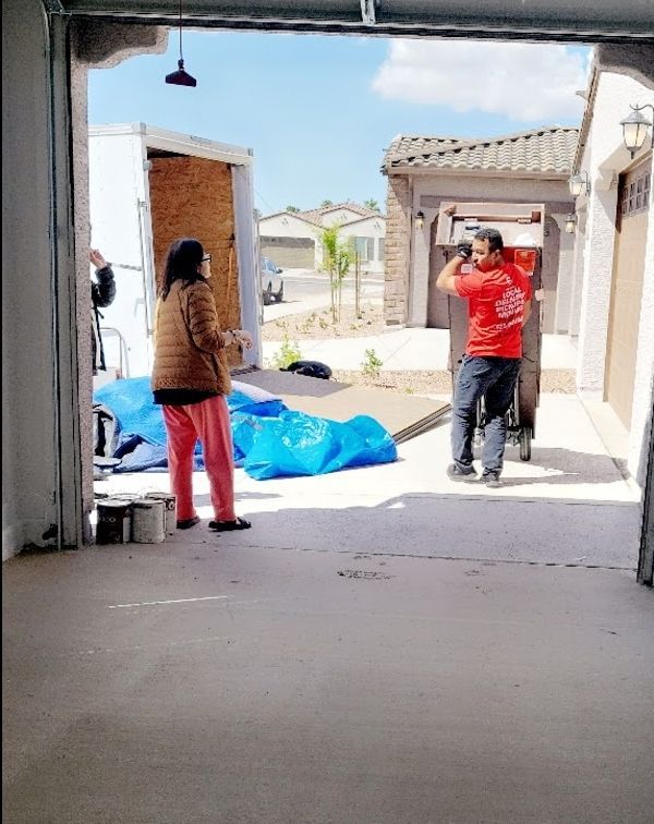 People loading items into a moving truck from a garage on a sunny day.