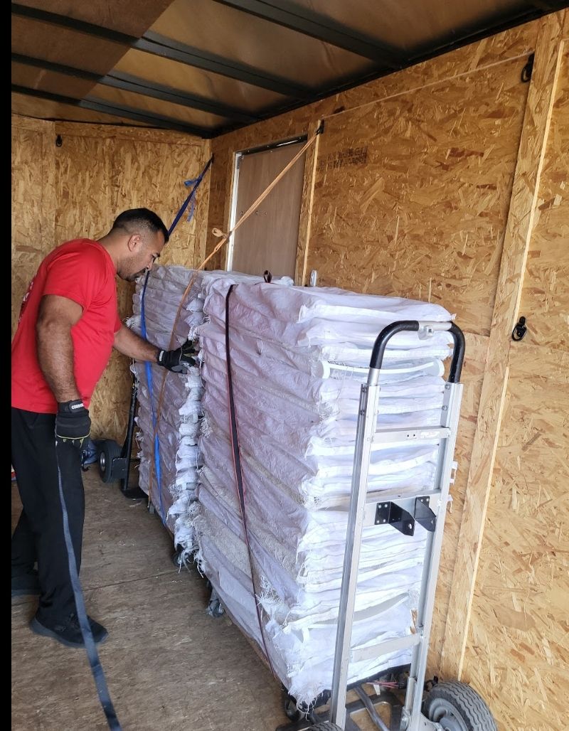 Man loading wrapped items onto a hand truck inside a wood-paneled trailer.