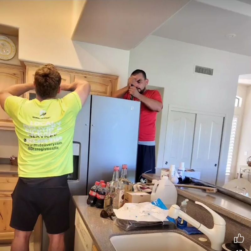 Two people installing a refrigerator in a kitchen. One person holds the fridge, another adjusts it.